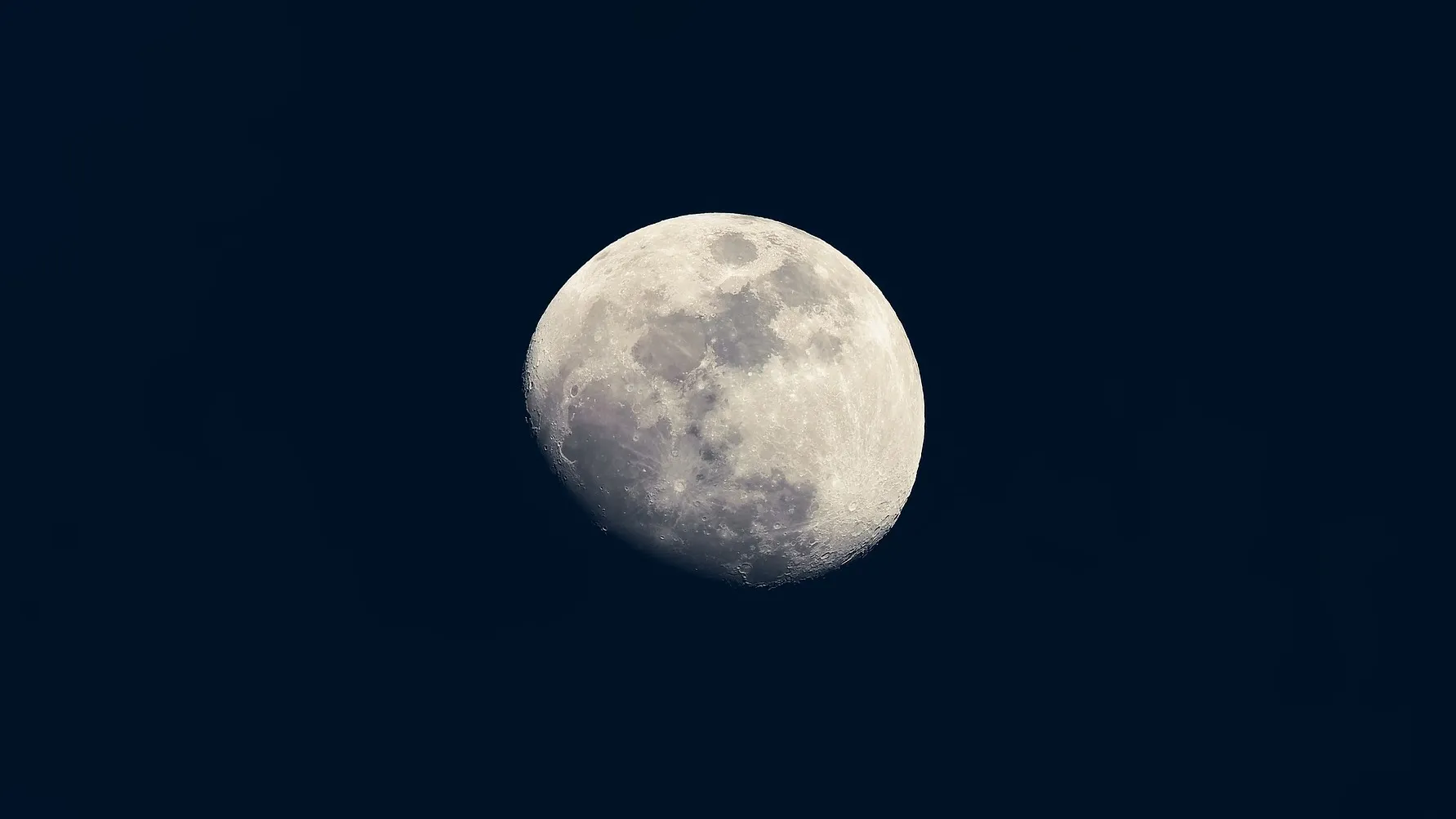The bright white Moon in its nearly full phase against a dark background. 