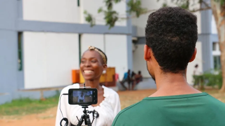 A man films a laughing woman using a cell phone camera on a tripod.