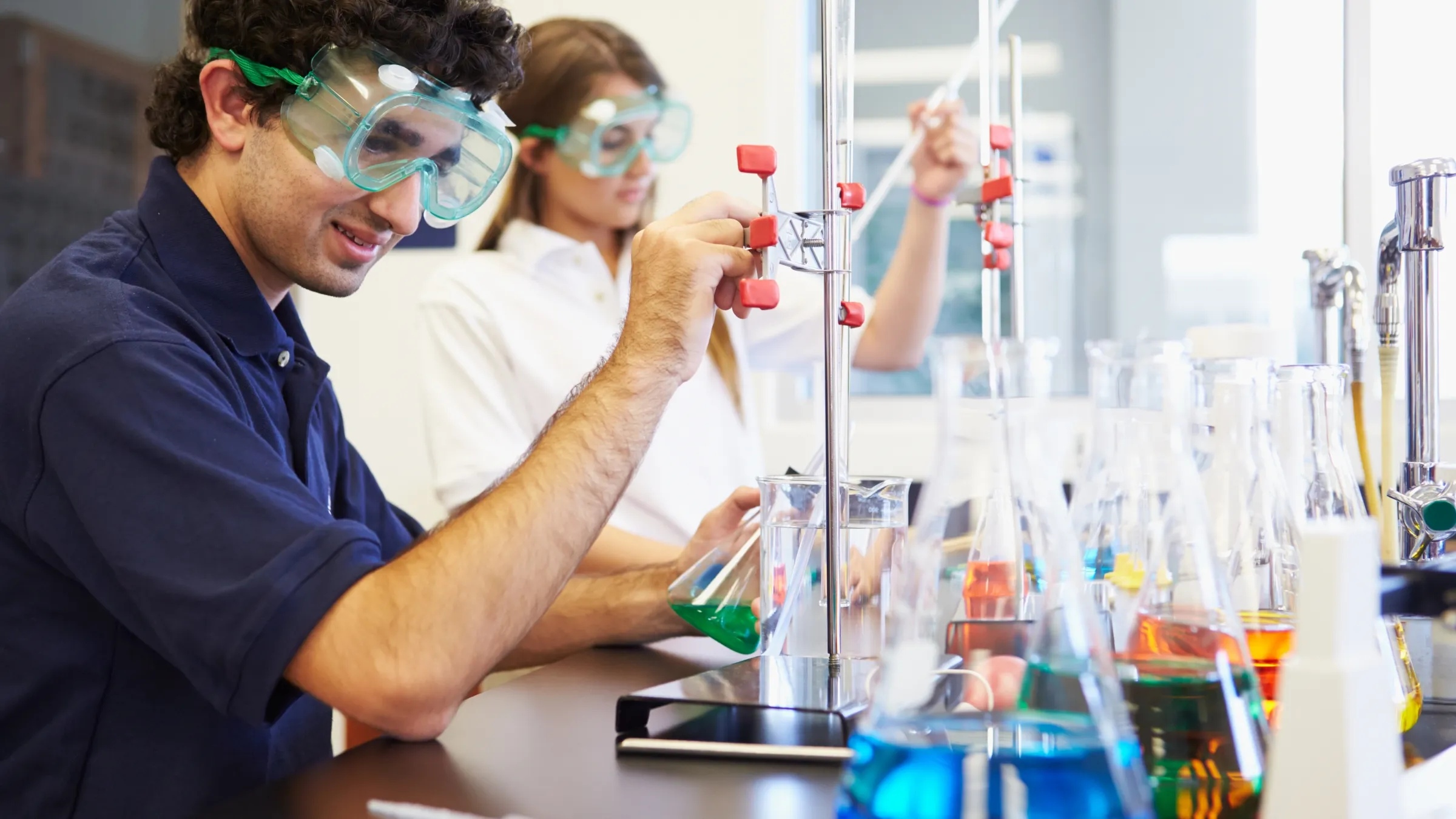 A chemistry student using a measuring cylinder to fill a beaker with chemicals.