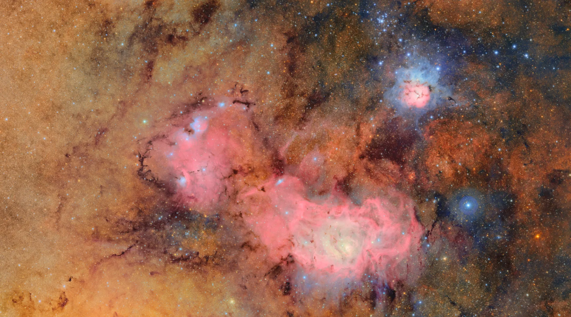 This composite of over 600 images shows the Trifid Nebula and the Lagoon Nebula, both bright pink and blue masses surrounded by orange clouds of dust and gases. Credit: NSF–DOE Vera C. Rubin Observatory.