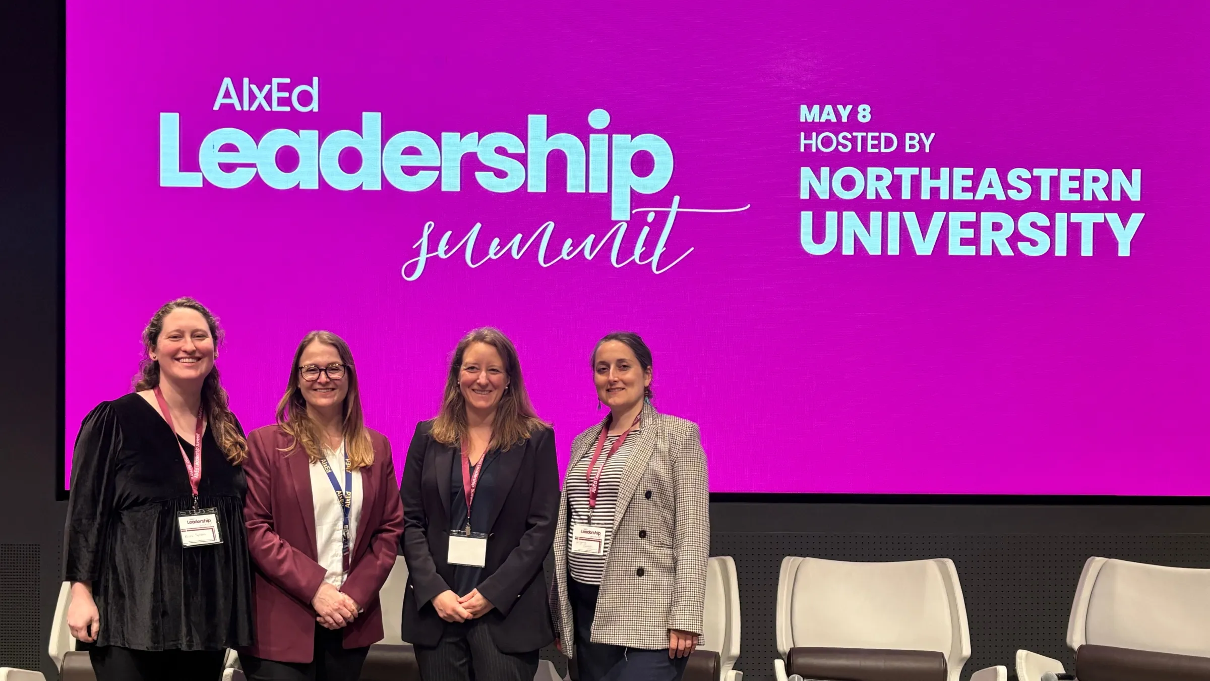 Four women stand in front of a screen with the text: "AIxEd Leadership Summit / May 8, Hosted by Northeastern University."