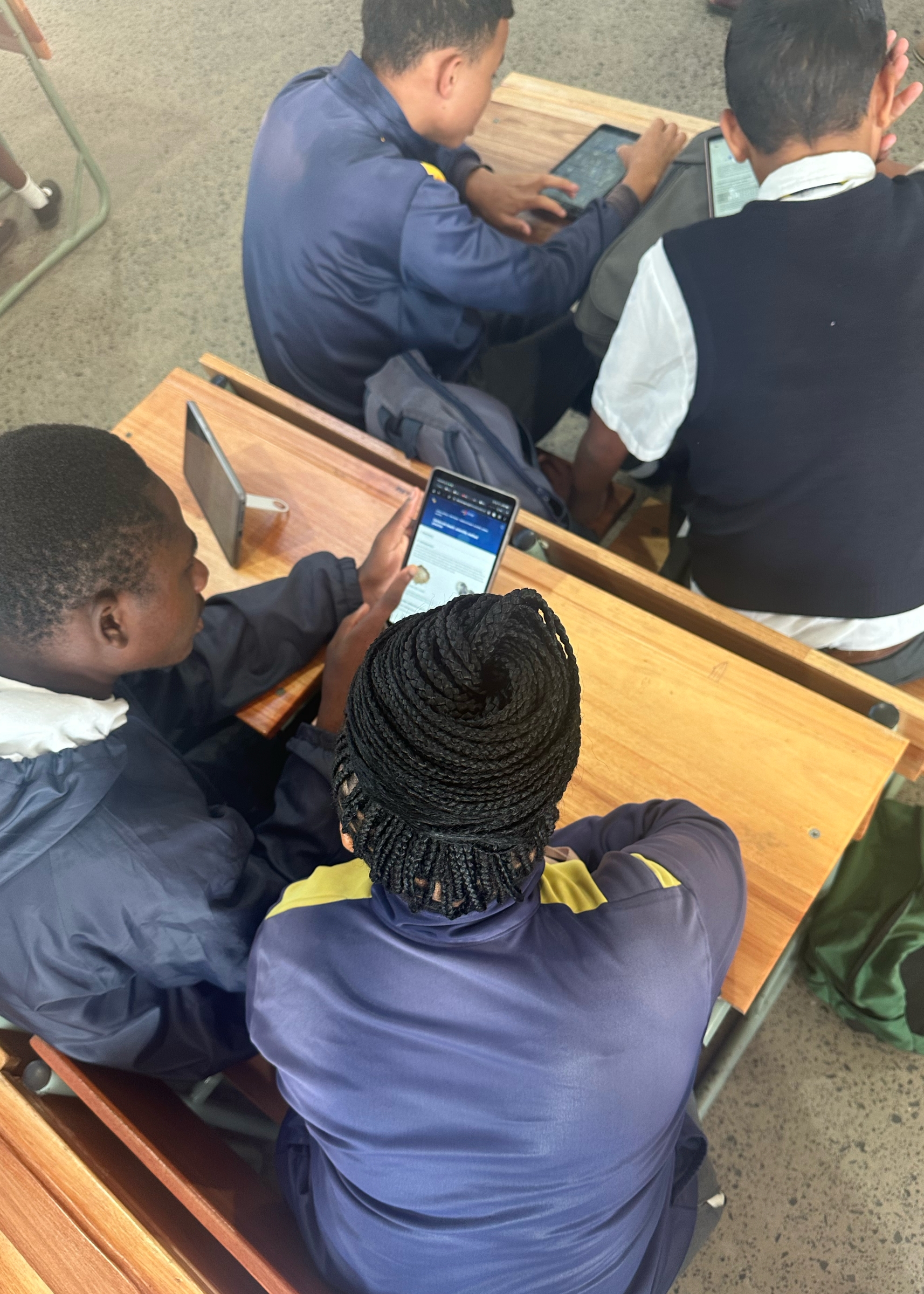 Crestway students in school uniforms sit at wooden desks using tablets and a smartphone to engage with LabXchange resources during a classroom activity.