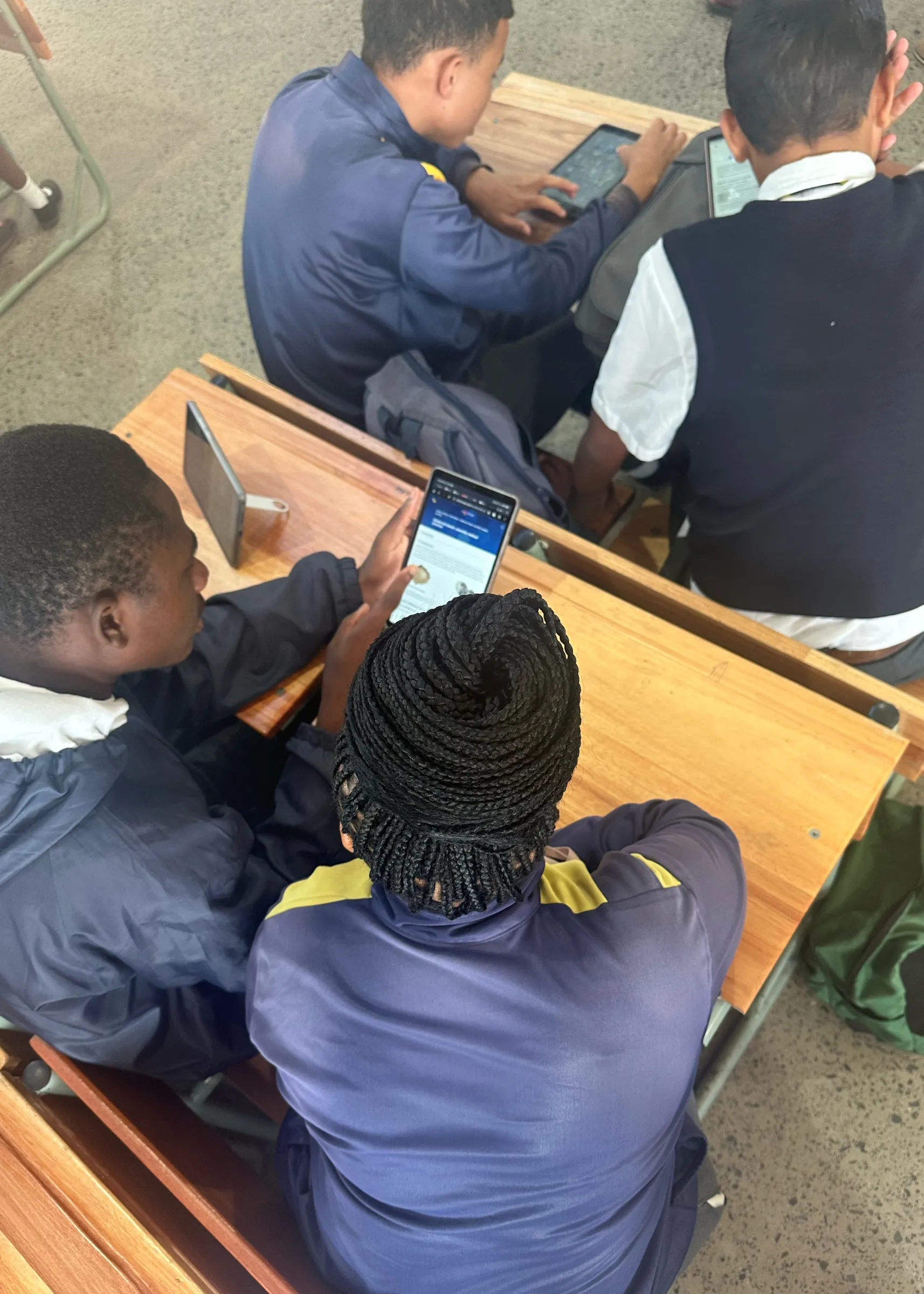 Crestway students in school uniforms sit at wooden desks using tablets and a smartphone to engage with LabXchange resources during a classroom activity.