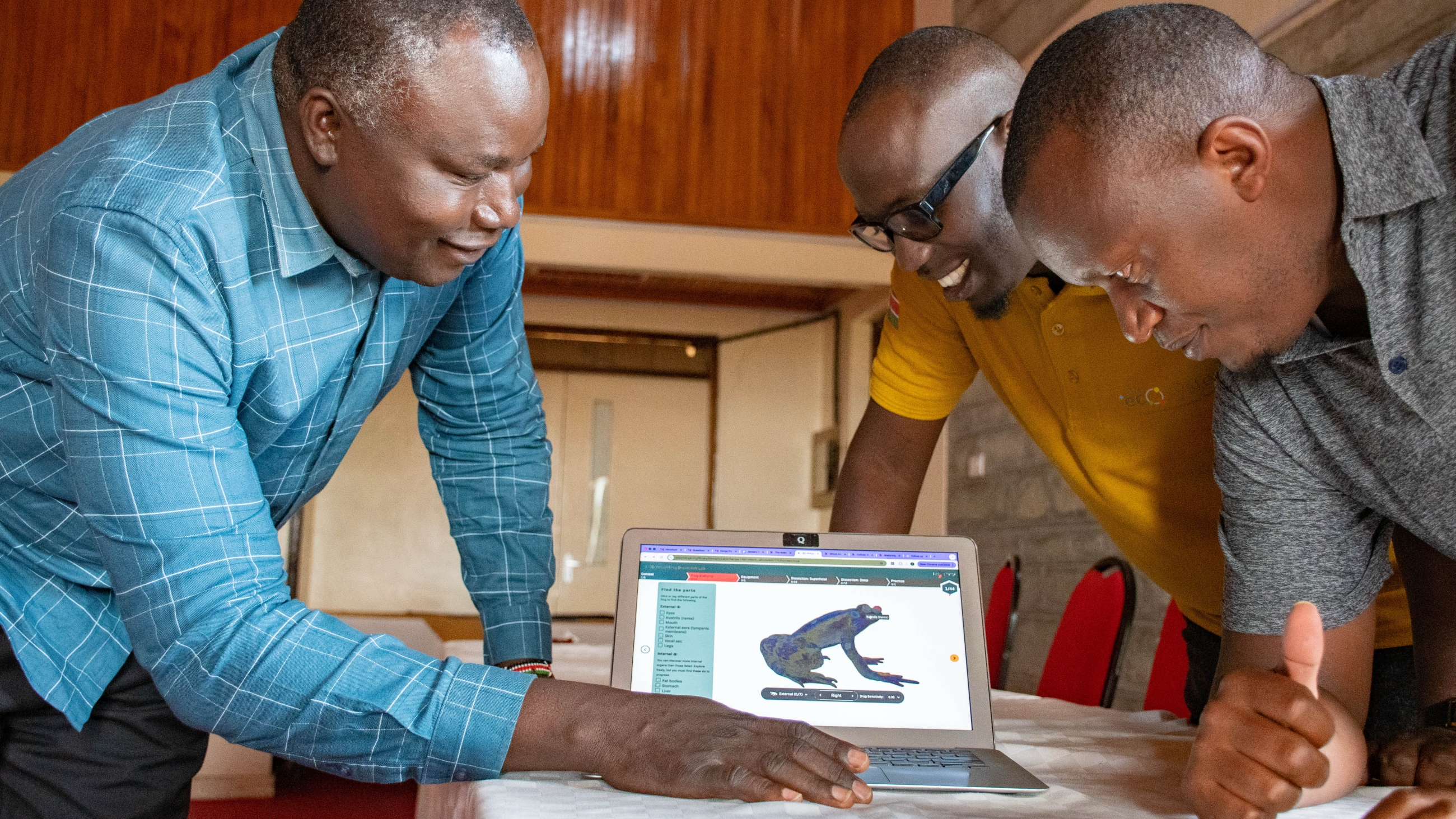 Three educators smiling and leaning over a laptop displaying a 3D frog anatomy model on LabXchange.org.