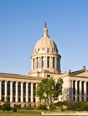 Classical government building with a large dome topped by a statue, surrounded by columns and green lawn under clear blue sky.
