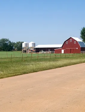 Red barn and white silos on a green farm field under a clear blue sky.