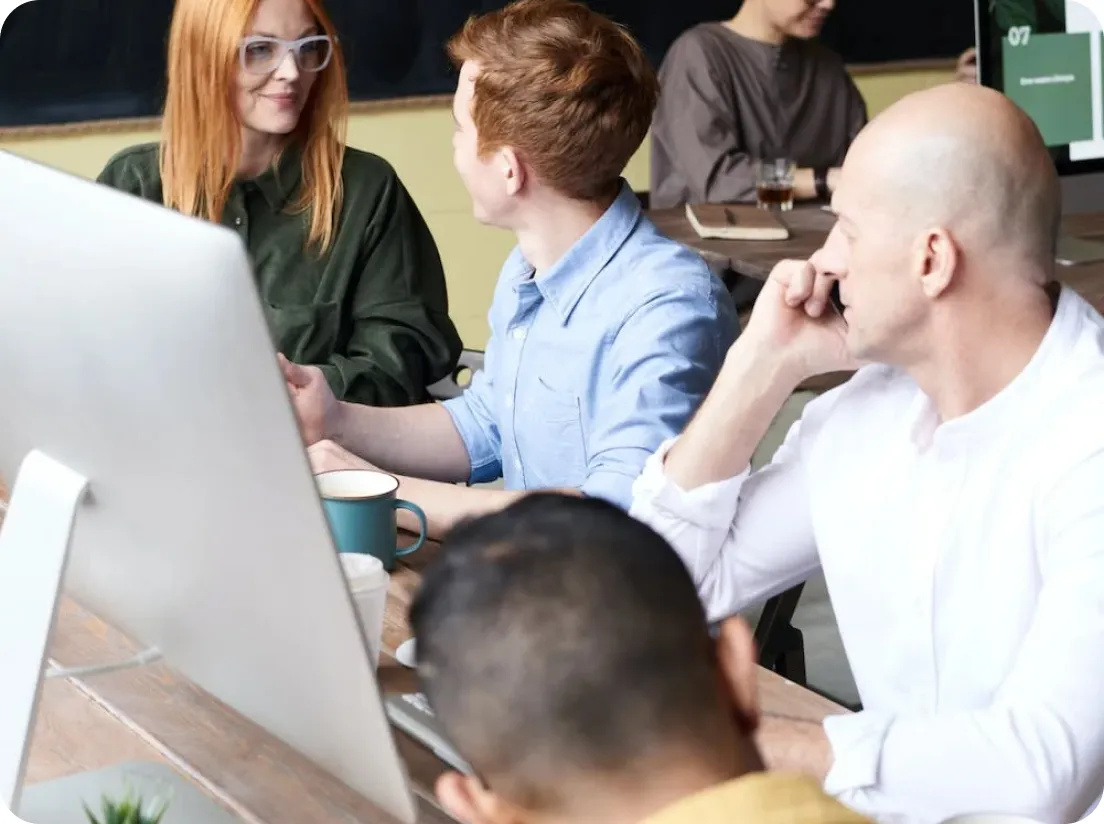 A group of people talking, sitting at a computer.