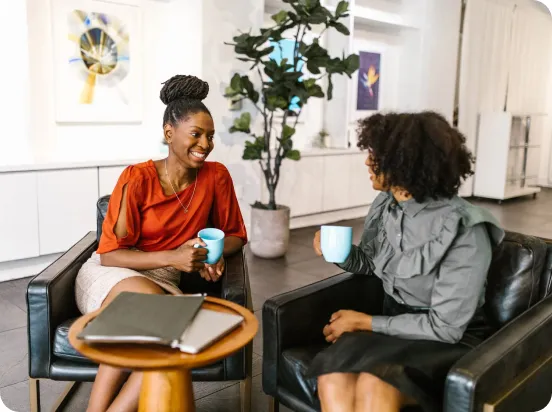 Two women laughing, drinking coffee, in an office