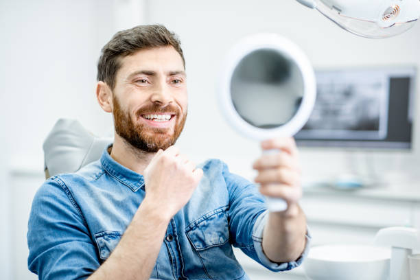 Man's portrait in the dental office Portrait of a handsome bearded man with healthy smile in the dental office  Adult man smiling confidently while looking into a mirror after veneers placement stock pictures, royalty-free photos & images