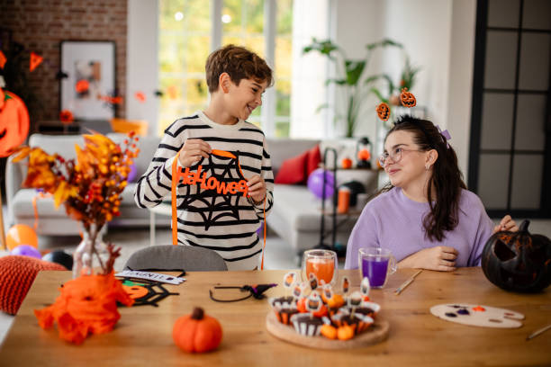 Joyful Halloween Crafting Fun Between Friends The image captures a charming moment where two friends create Halloween crafts while sharing smiles and laughter, embodying the spirit of the festive season. family sorting Halloween candy on the kitchen table with smiles stock pictures, royalty-free photos & images