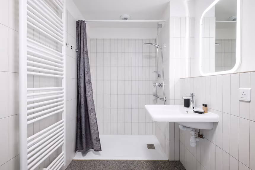 Salle d'eau carrelée avec douche, lavabo suspendu, miroir lumineux et sèche-serviettes