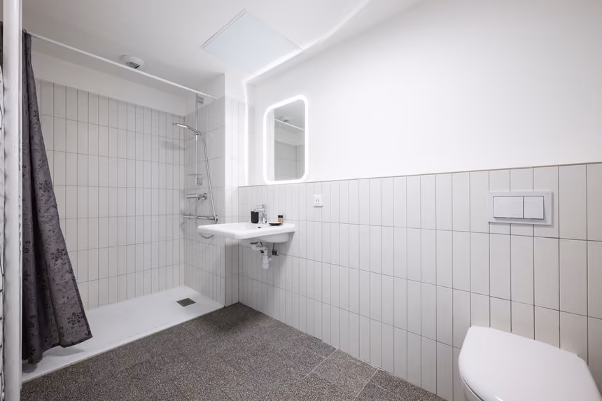 Salle d'eau de l'appartement de 29 m² : douche, lavabo, miroir lumineux et WC suspendu