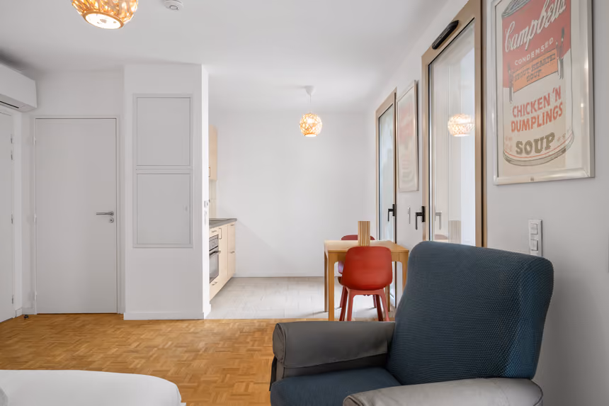 Séjour de l'appartement de 29 m² avec fauteuil de lecture, coin repas et porte-fenêtre