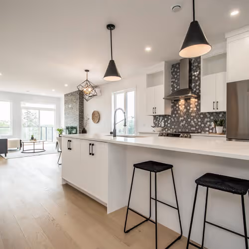 Home construction nova scotia -Modern kitchen with white cabinetry, black pendant lights, hexagonal patterned backsplash, and two black bar stools at the island counter. Home builder in Halifax, Nova Scotia.
