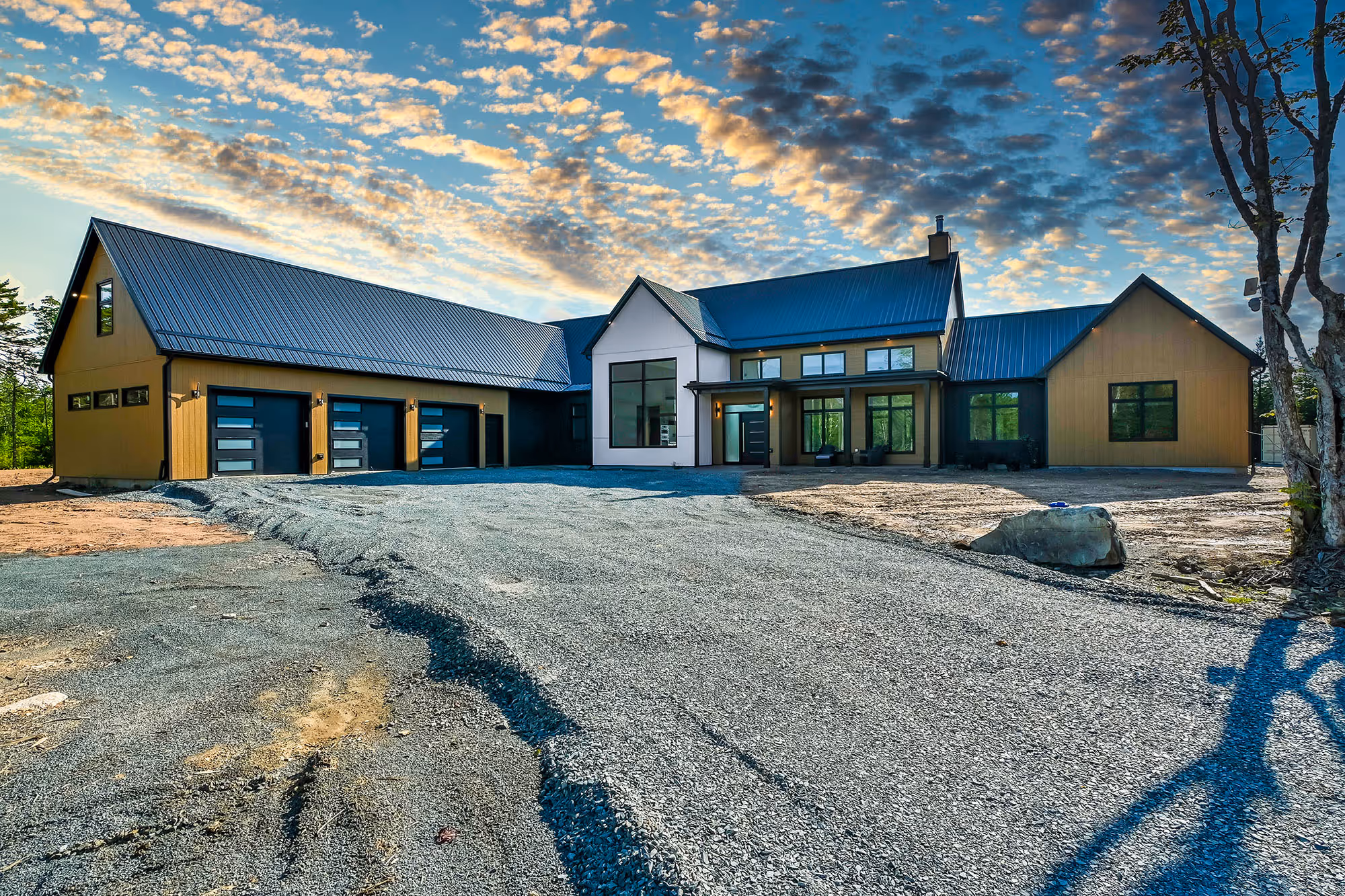 Signature homes builder -Home builders in Halifax: Signature Homes - Modern large house with yellow and black exterior, multiple garage doors, and a gravel driveway under a dramatic sky with scattered clouds.