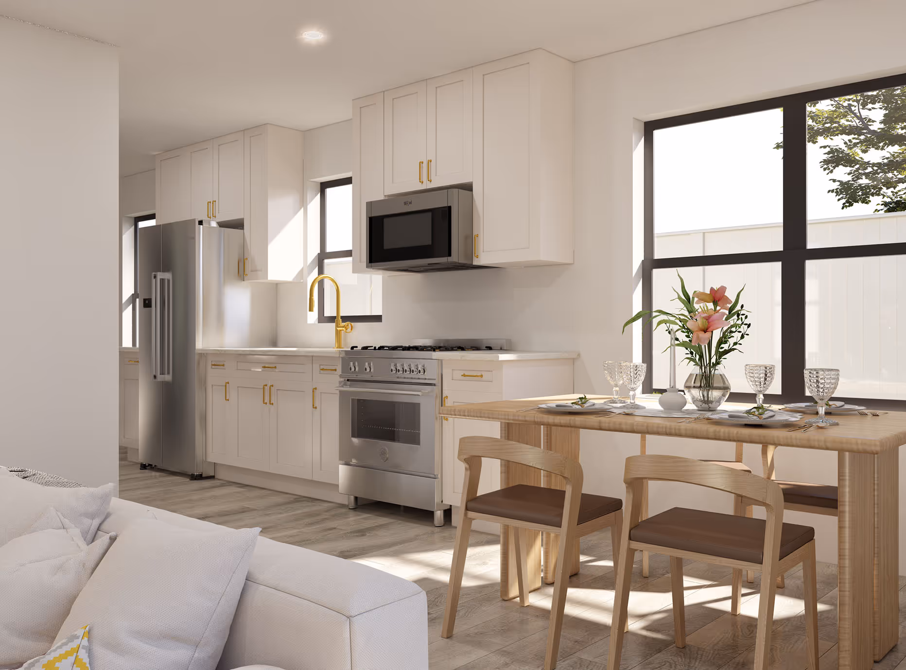 Bright kitchen with white cabinets, stainless steel appliances, gold fixtures, and a wood dining table set with flowers and glassware near large windows.