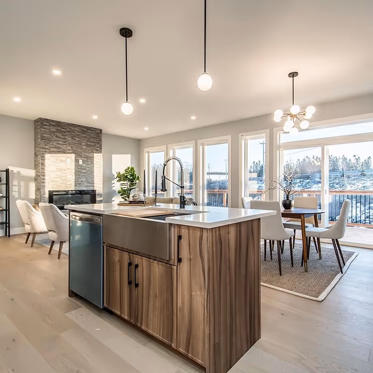 Modern kitchen with large wooden island featuring a farmhouse sink, pendant lights, stone fireplace, and dining area with large windows in Halifax Nova Scotia. Signature Home Builders.