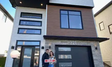 Modern two-story house with white and brown exterior, large windows, and a couple standing in front holding a SOLD sign. Signature Home Builders in Halifax, Nova Scotia