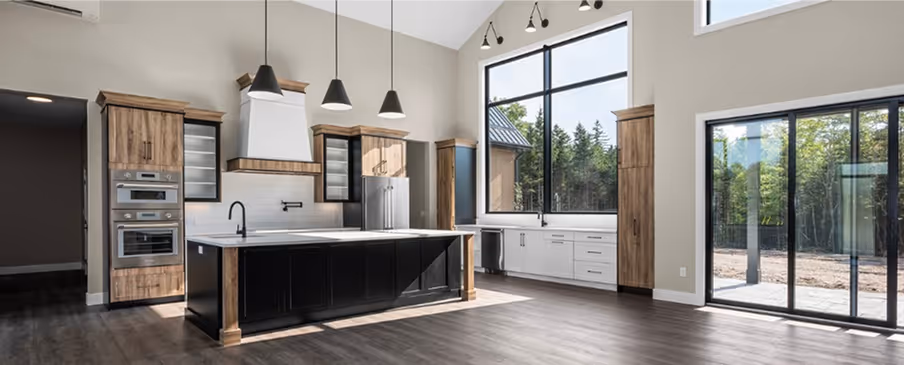 Custom modern kitchen with large island featuring dark cabinetry, wooden cabinets, stainless steel appliances, and large windows overlooking a wooded yard. Signature Homes