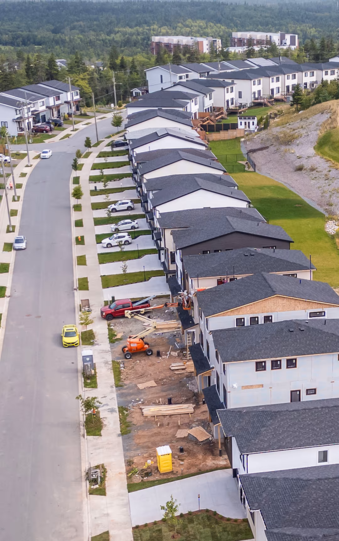 Aerial view of a new residential neighbourhood in Nova Scotia with rows of modern homes, driveways, and forested hills in the background