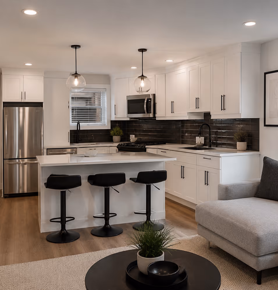 Open-concept ADU kitchen and living area in Halifax featuring white cabinetry, stainless steel appliances, island seating, and modern pendant lighting by SignatureHome