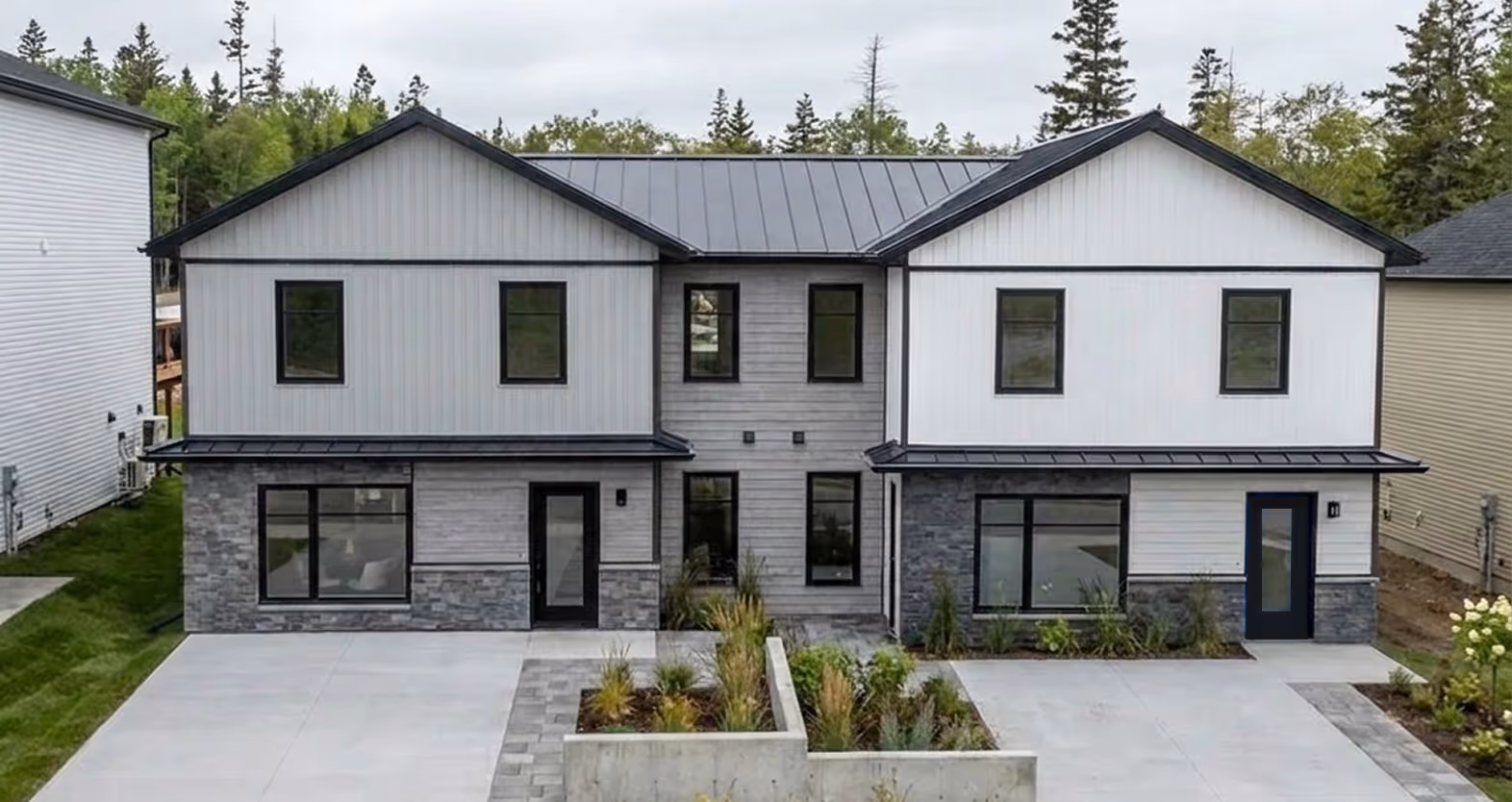 Modern duplex home with black garage doors, stone and siding exterior, manicured landscaping, and contemporary design in Halifax