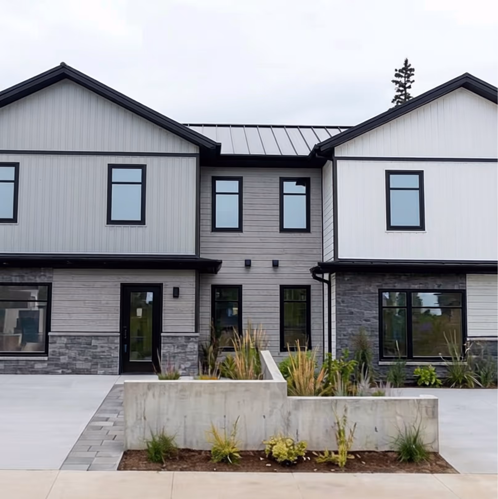 Aerial view of duplex home with modern metal roof, concrete driveway, wooded forest backdrop, and residential landscaping in Halifax area