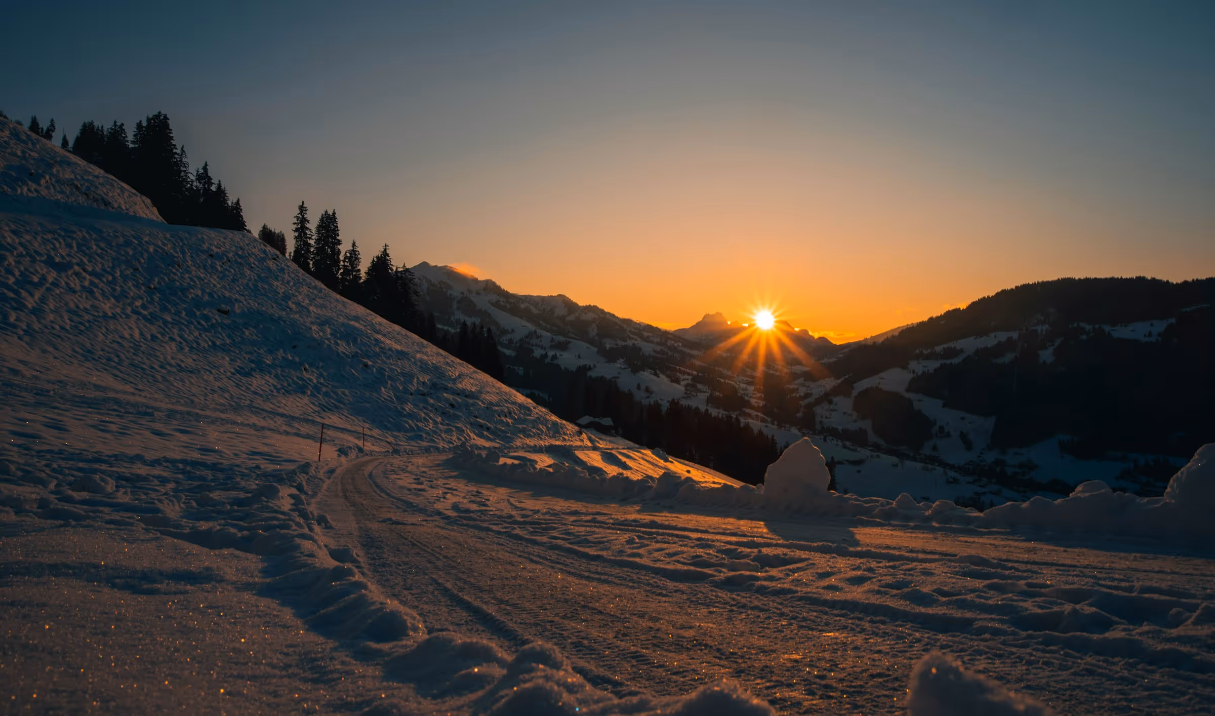 Sonnenuntergang in verschneiten Bergen mit schneebedeckter Straße und Tannenzapfen.