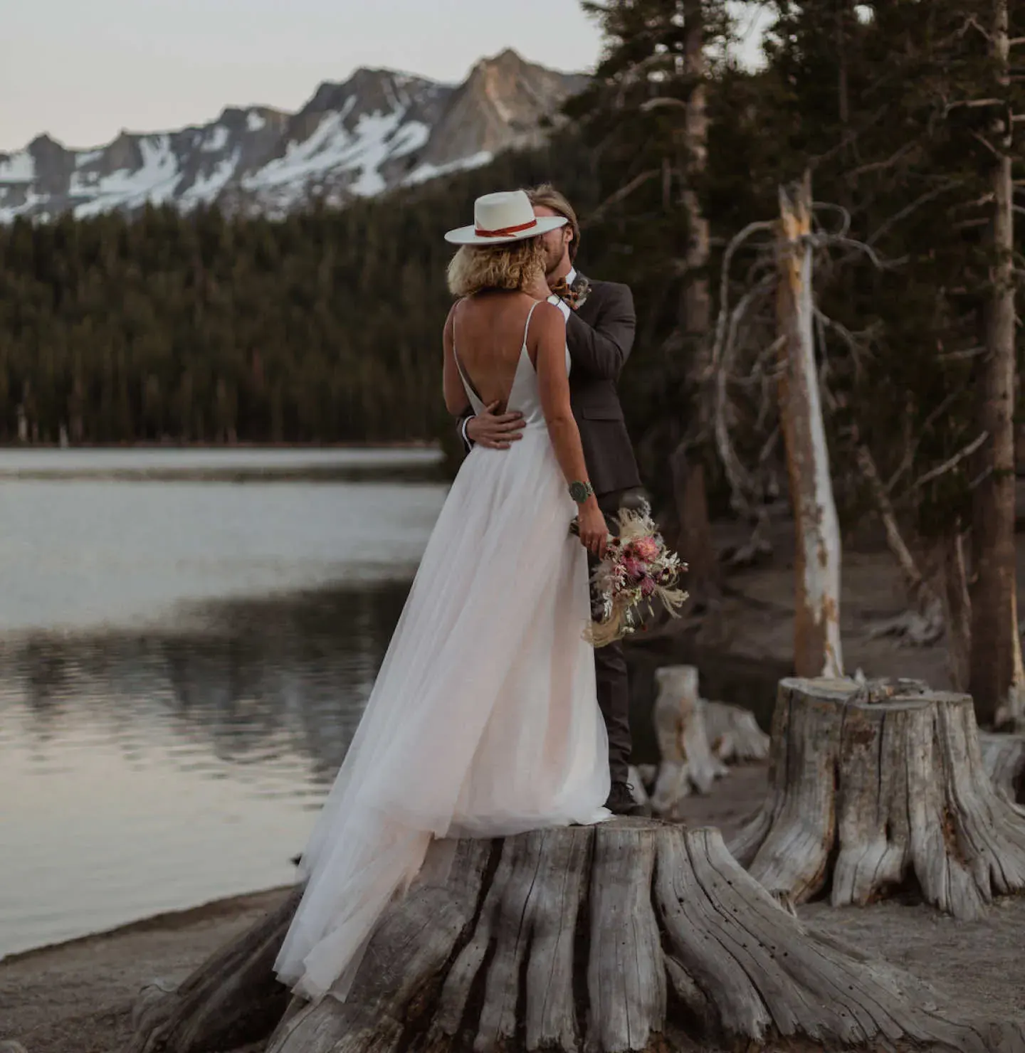 Boho bride and groom standing on a tree stump next to a lake