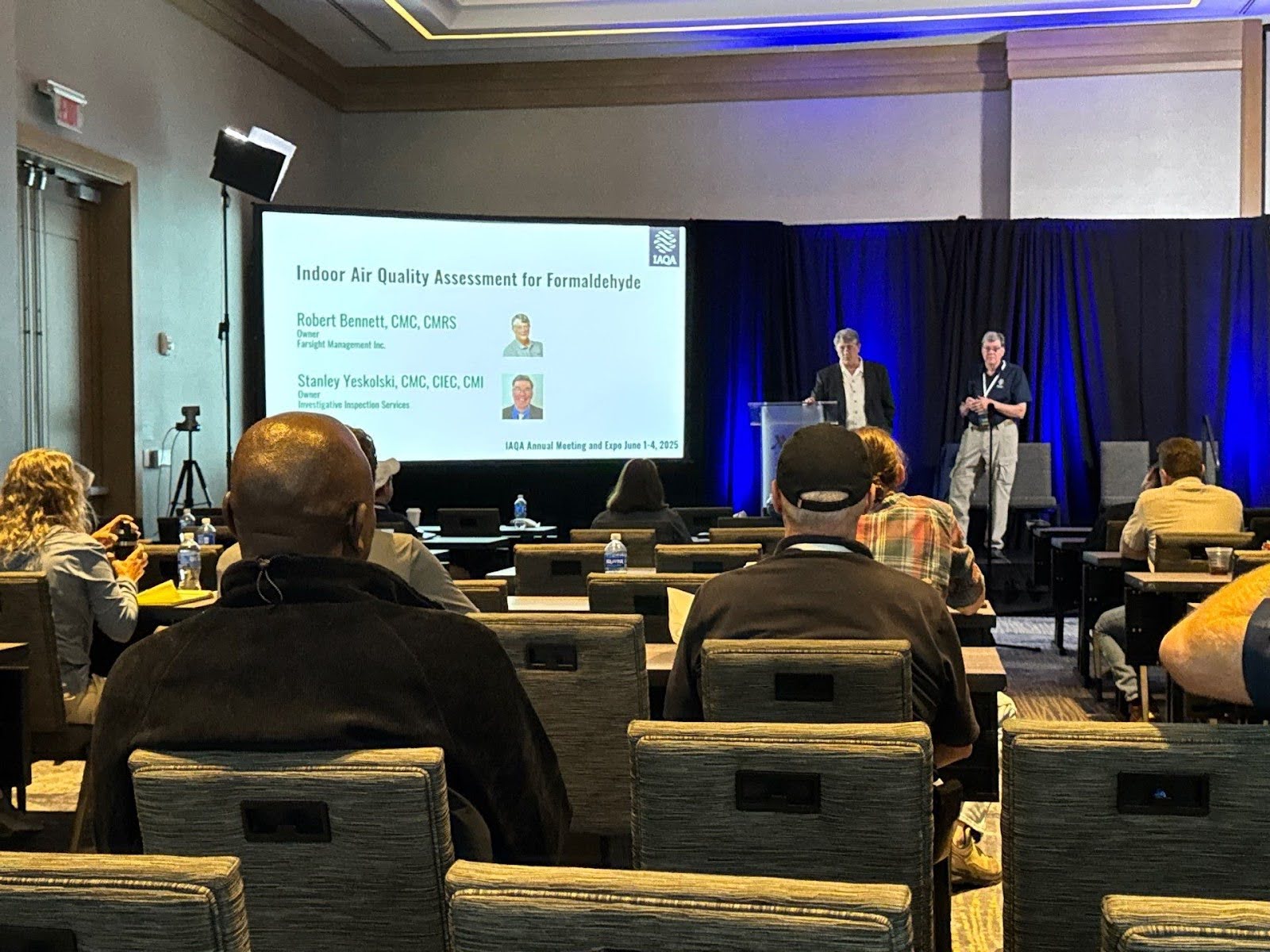 wide view from someone sitting in the audience looking at 2 men presenting on stage