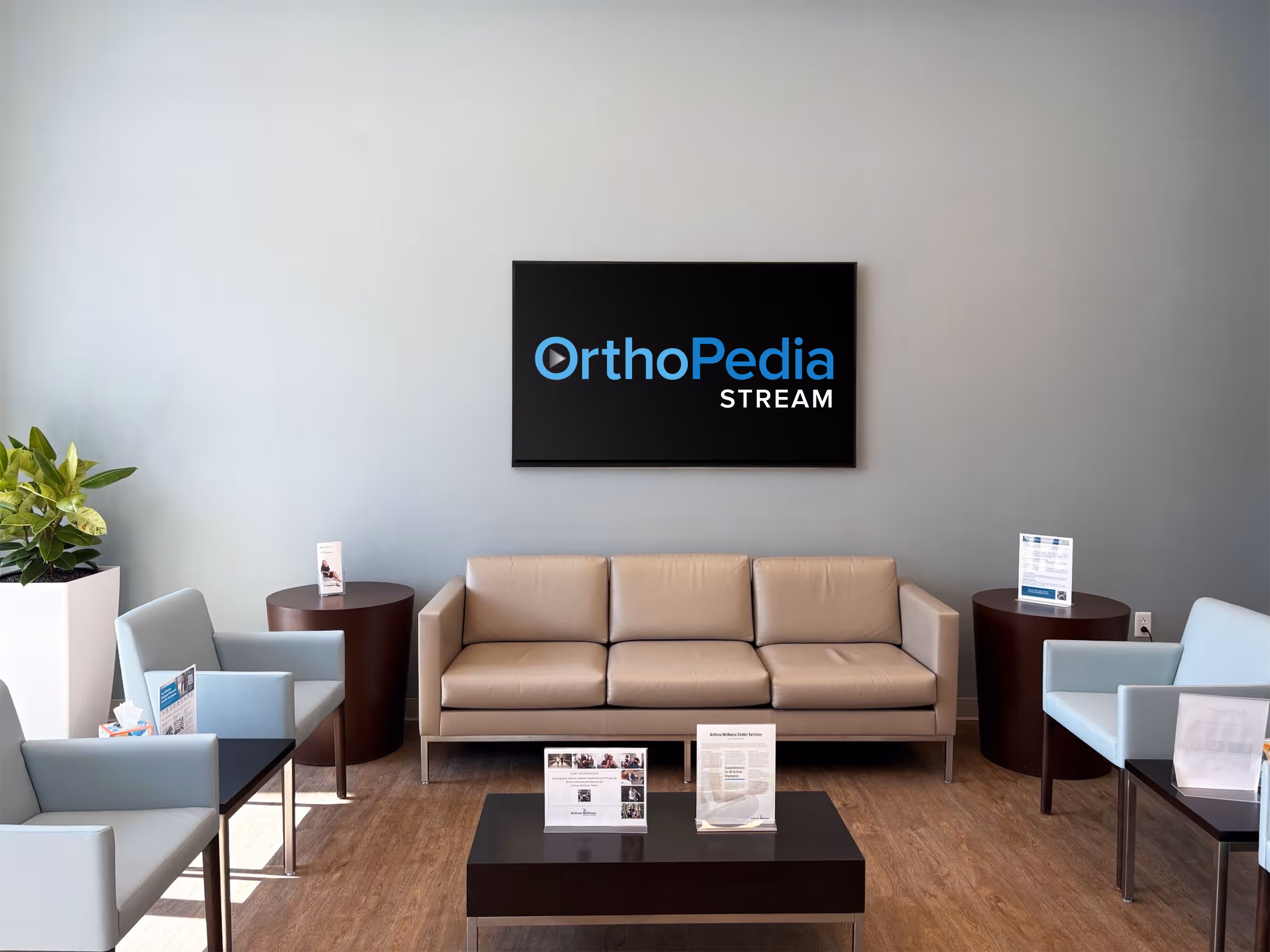 Modern waiting area with chairs and a couch, featuring a wall-mounted screen displaying the OrthoPedia Stream logo.