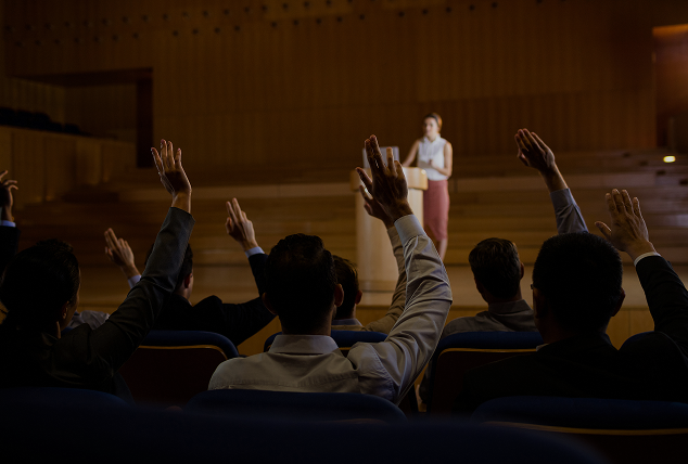 Smiling man with short brown hair and light stubble wearing a white shirt against a wooden panel background.