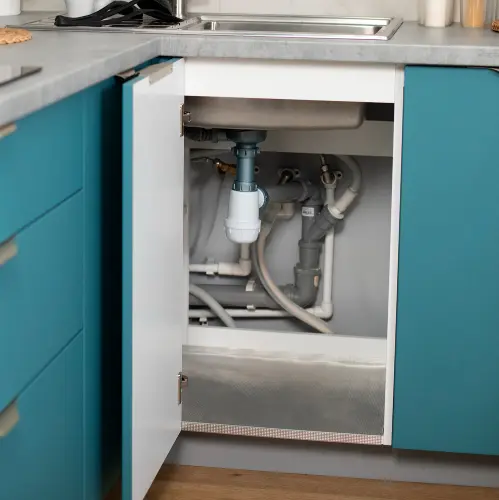Open kitchen cabinet under sink showing plumbing pipes and drain fittings in a modern kitchen.