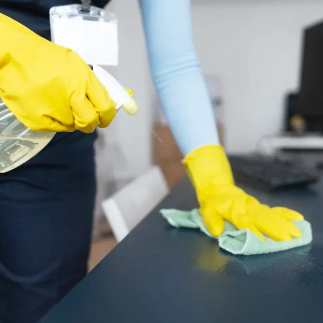 Person wearing yellow gloves cleaning a dark surface with spray bottle and cloth.