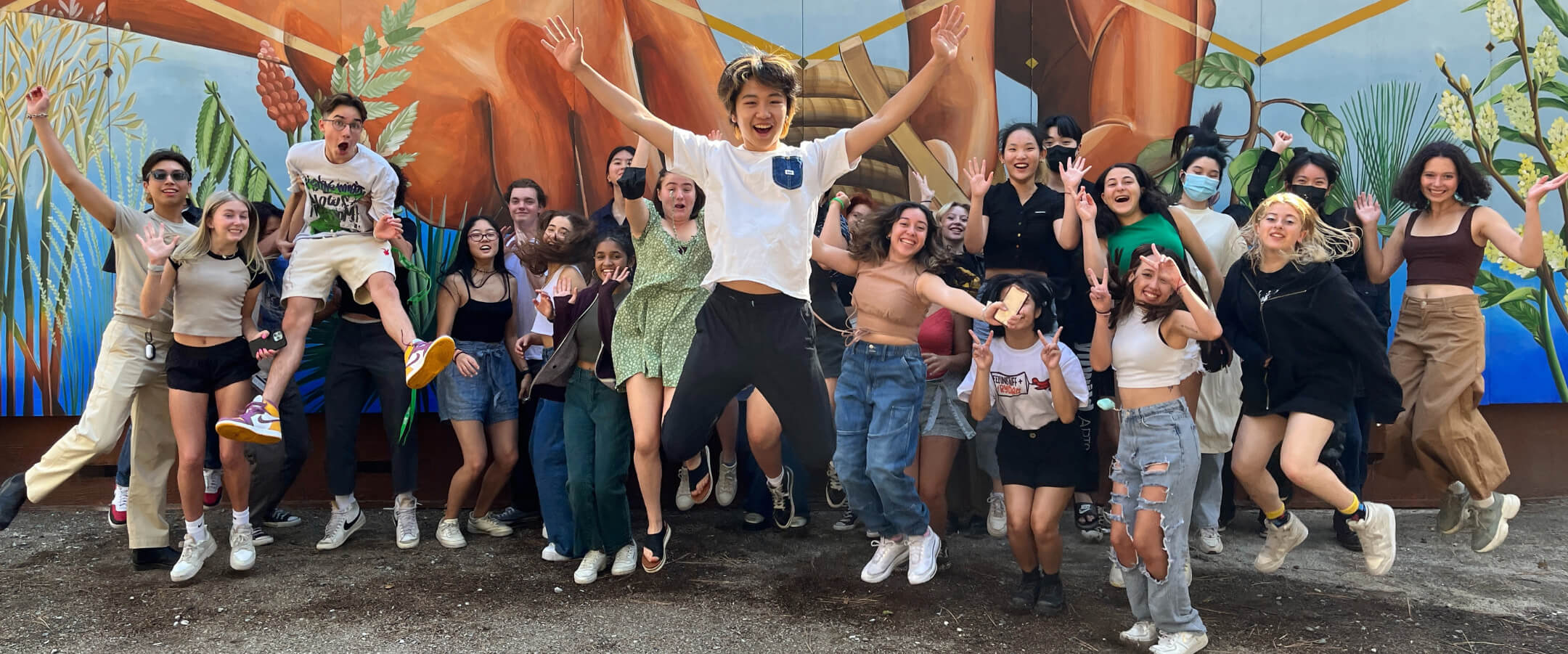 Idyllwild Arts Academy jumping and cheering in front of a large wall mural.