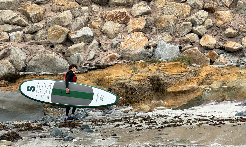 A Stevenson School student carrying a stand up paddle board along the shoreline.