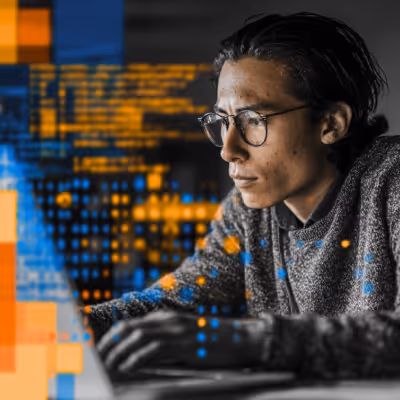 Person wearing glasses and a gray sweater focused on working at a computer with digital data overlays.