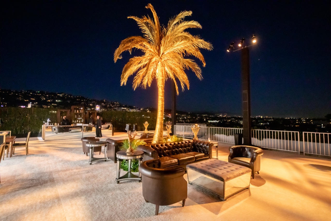 Impact illuminated a palm tree over a rooftop lounge with leather seating overlooking the Los Angeles skyline at night.