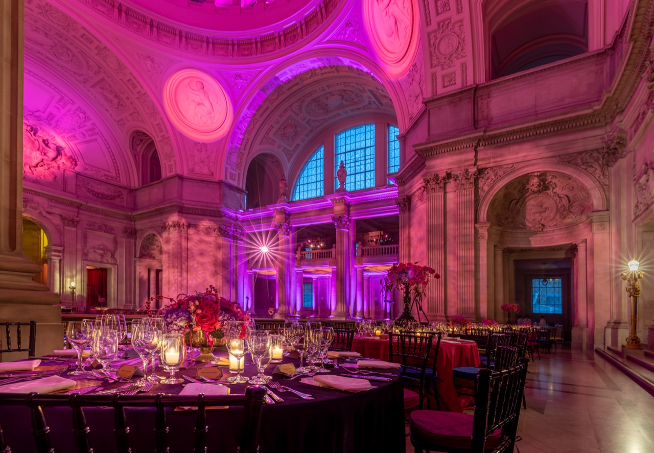 The City Hall rotunda bathed in amethyst uplight with candlelit tables and a radiant starburst fixture, lit by Impact.