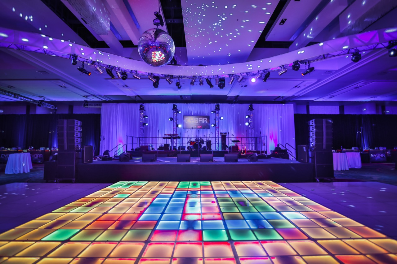 A multicolor LED dance floor and mirror ball anchor a corporate after-party stage draped and lit by Impact.