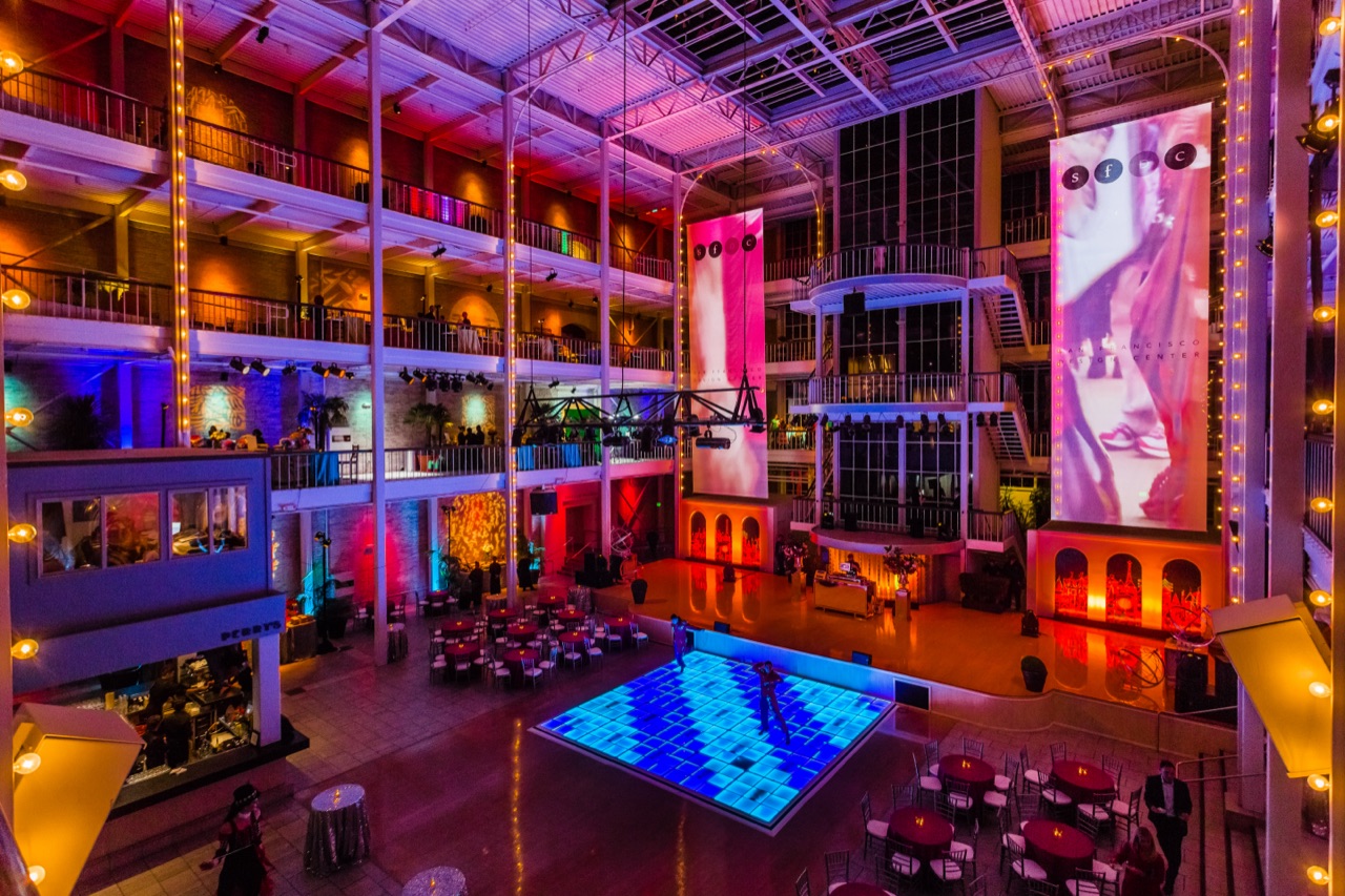 Impact's glowing LED dance floor, uplighting, and hanging banners transform a grand multi-story atrium.