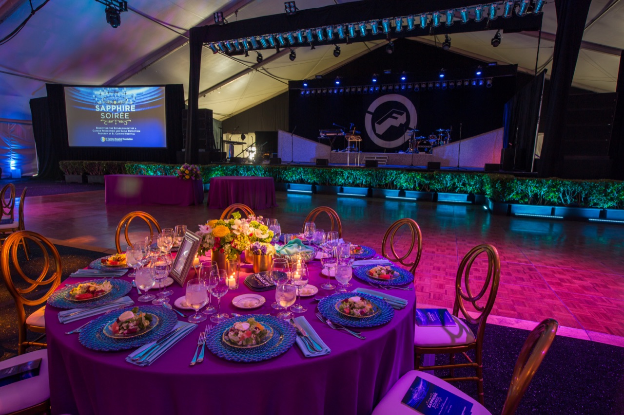 Impact's purple uplighting, green stage wash, and band lighting set a tented gala with a formal foreground dinner table.
