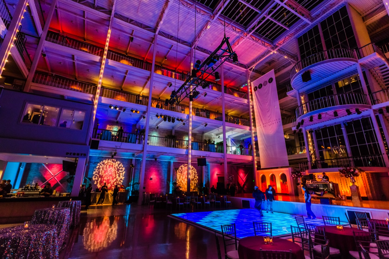 Impact's red and blue architectural uplighting, patterned gobos, and a glowing blue LED dance floor fill a multi-story atrium.