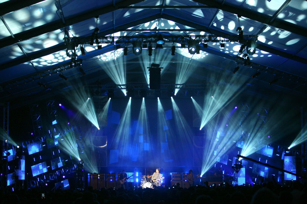 A performer on a tented stage bathed in Impact's blue beams and haze, with LED panels and light columns filling the structure.