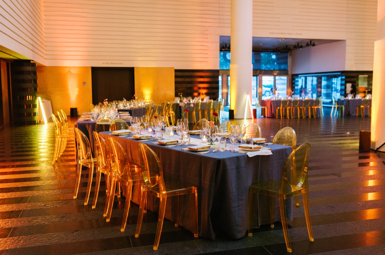 Impact washed the SFMOMA atrium in warm amber uplighting for a seated dinner with ghost chairs and long tables.