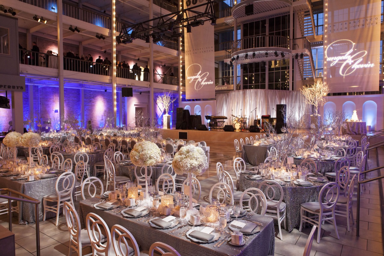 Impact fills a grand columned hall with purple and blue uplighting, a lit stage for the band, and monogram gobo banners over silver-sequin banquet tables.