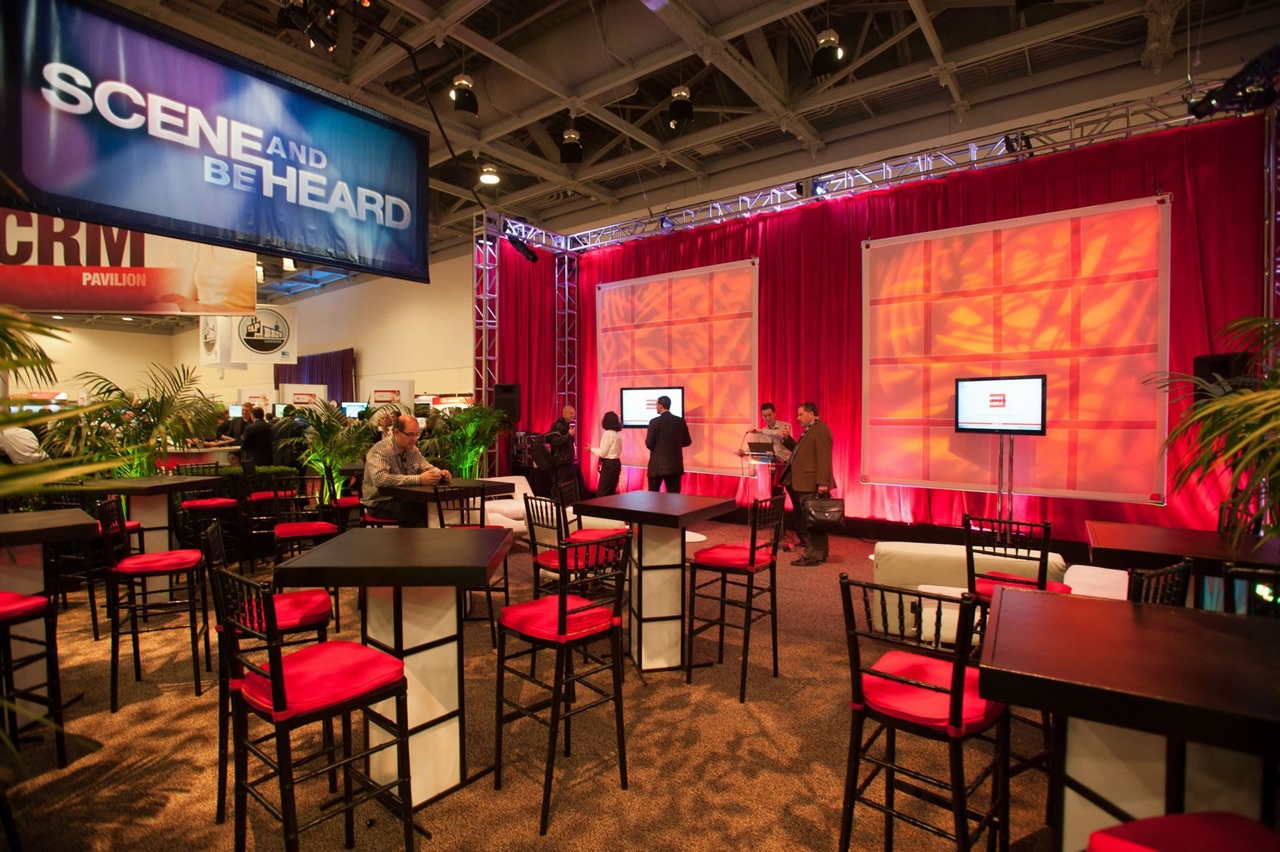 Impact uplit a red-draped Oracle trade show pavilion with truss-mounted lighting, monitor displays, and cocktail seating.
