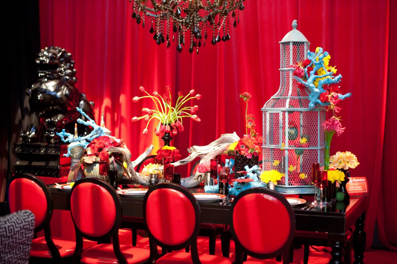 A dramatic red-draped tablescape with a black crystal chandelier and vivid floral decor, backed by Impact's crimson drape wash.