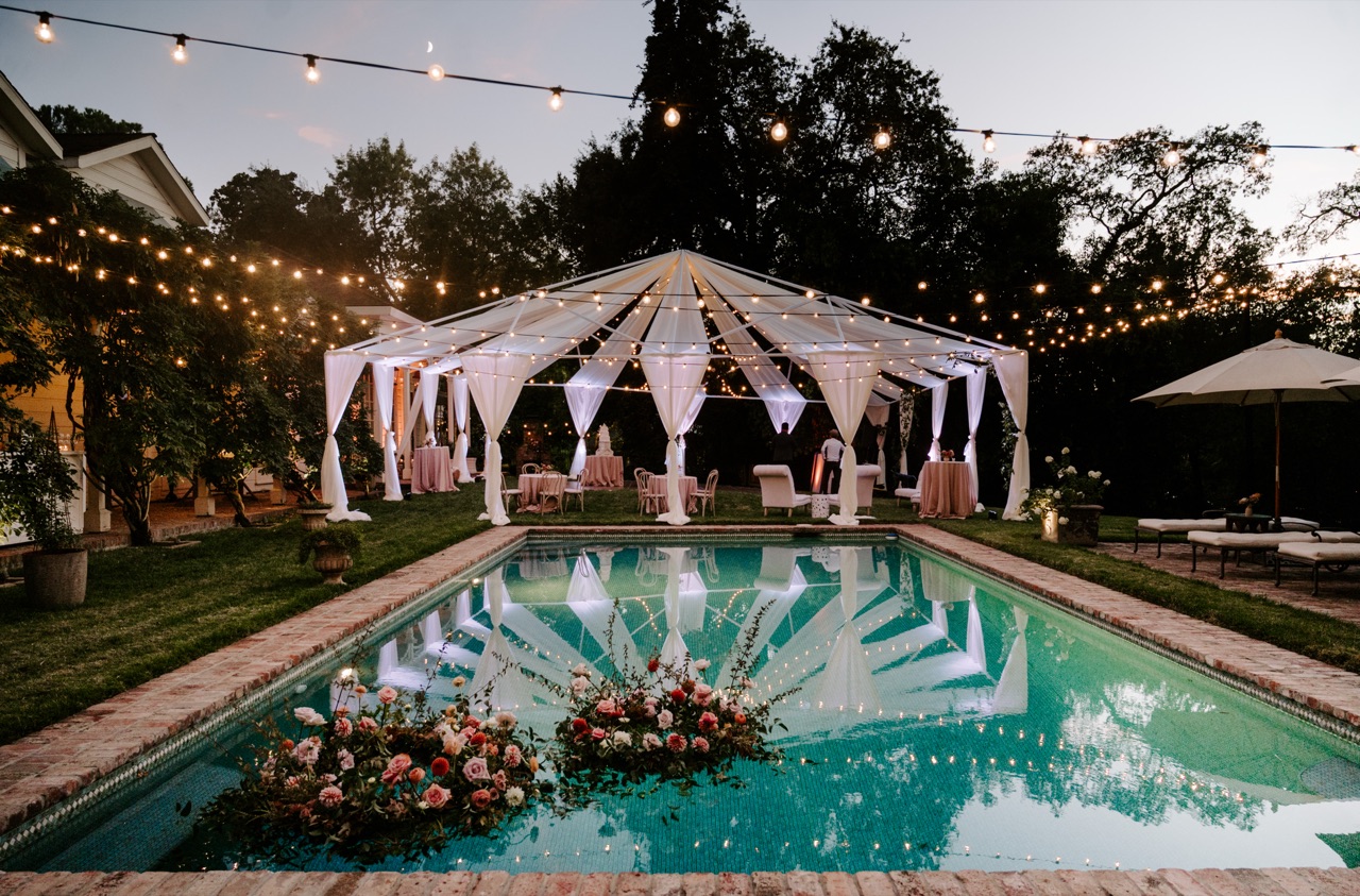 Impact drapes a garden pool with crisscrossed bistro lighting and an illuminated clear tent, its glow mirrored in the water at a Carmichael estate wedding.