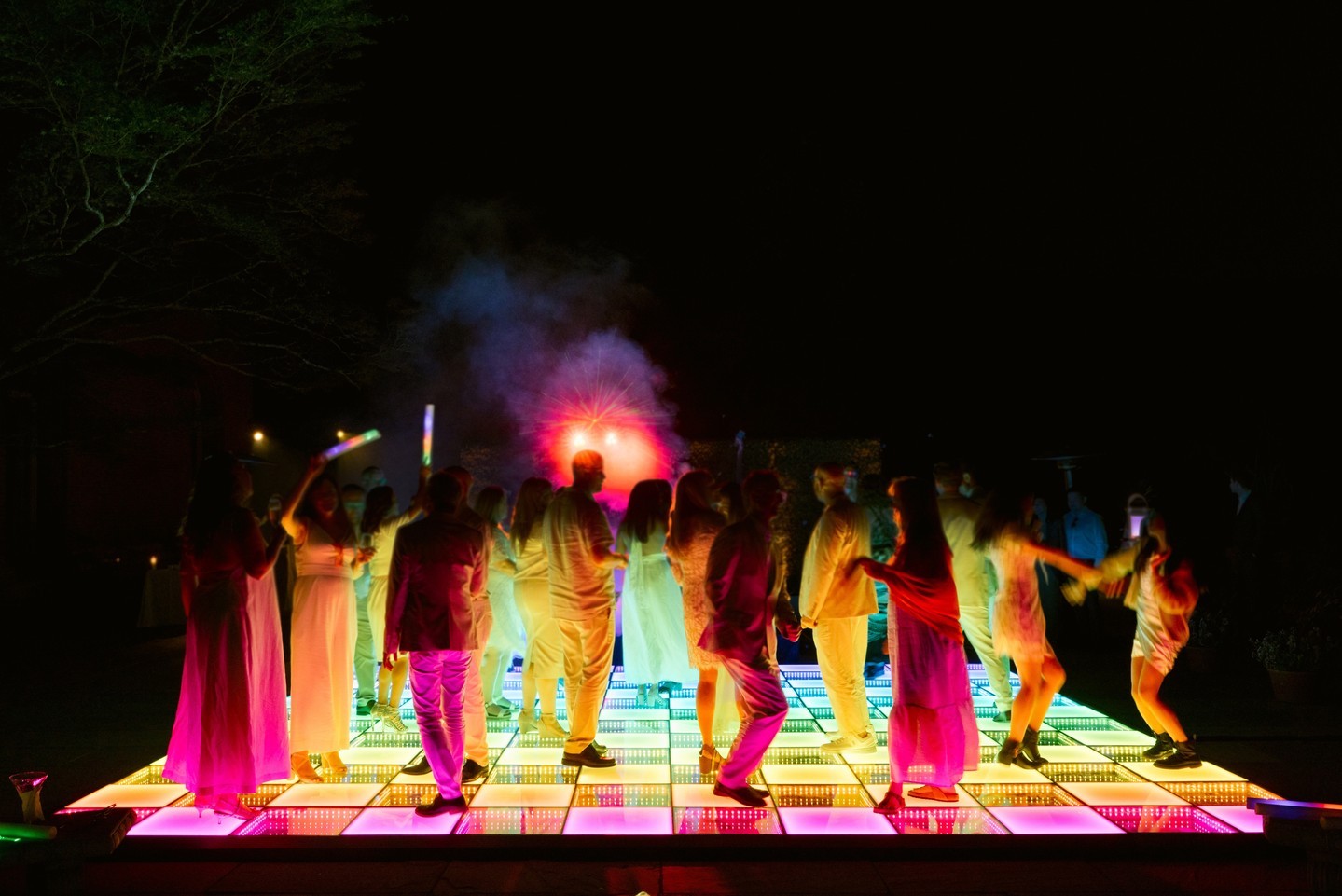 Guests dancing at night on a multicolor infinity dance floor at an outdoor celebration